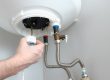 The,Hand,Of,A,Plumber,Installs,A,Thermostat,In,A