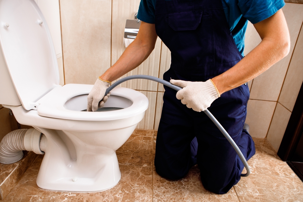 Plumber,Unclogging,Blocked,Toilet,With,Hydro,Jetting,At,Home,Bathroom. Plumber,Unclogging,Blocked,Toilet,With,Hydro,Jetting,At,Home,Bathroom.